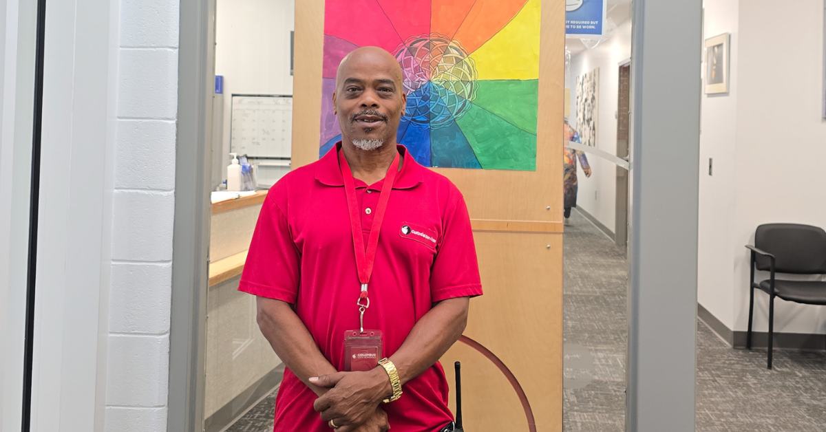 man wearing red shirt smiling in front of rainbow painting